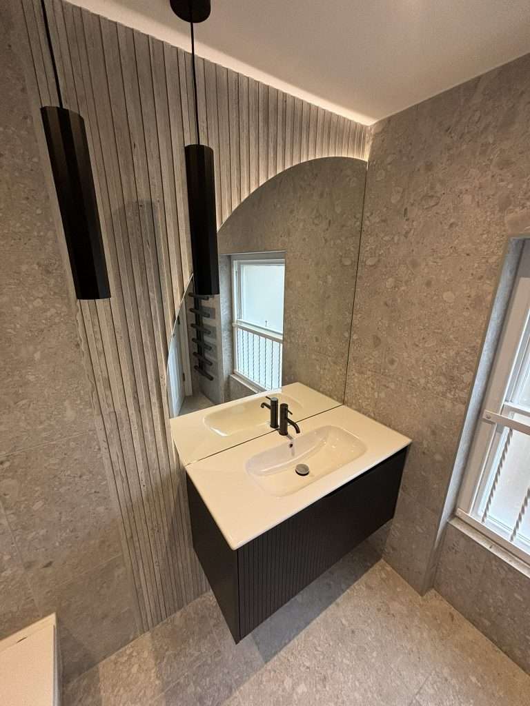 Modern bathroom renovation with floating black vanity, illuminated mirror and fluted grey tiles
