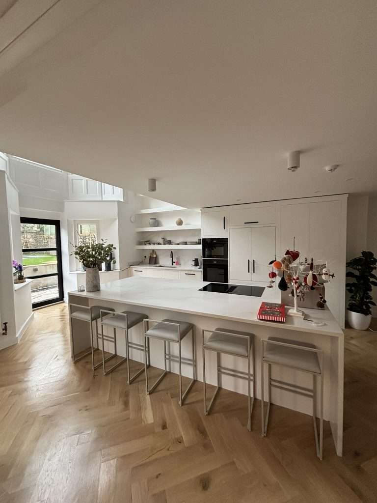 White kitchen renovation with large island and herringbone wood flooring